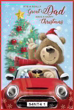 A teddy bear drives a red car with a Christmas tree in the background.