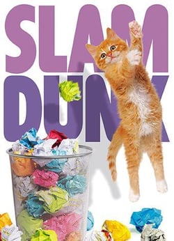 a kitten is jumping over a trash can filled with crumpled paper .