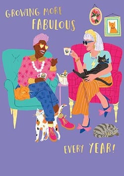 two women are sitting in chairs with cats and drinking tea .