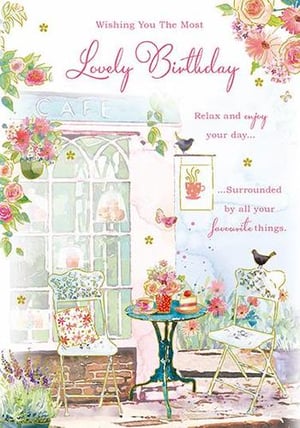 A birthday card with a table and chairs is in front of a cafe.