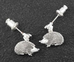a pair of silver hedgehog stud earrings on a black surface .