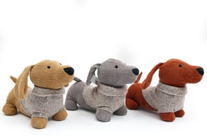 Introduce a touch of playful charm to any home with our delightful Dog Doorstops. This charming trio features three adorable dachshunds, each sporting a cosy knitted sweater. Crafted with a lovely corduroy-textured body in assorted colours – a warm tan, a sophisticated grey, and a rich rust – these doorstops are designed to add character and functionality. Their sturdy build ensures doors stay open with ease, while their endearing design makes them a wonderful decorative accent. Perfect for adding a friendly face to any room, these doorstops are sold as a convenient pack of three, offering variety and style for your customers.