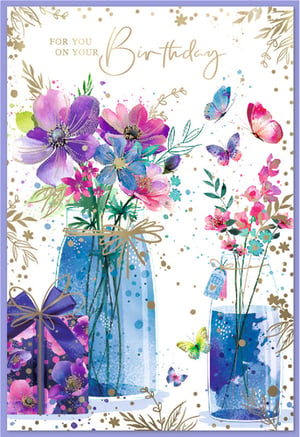 Send your warmest wishes with this exquisite Birthday card, perfect for any special woman in your life. This stunning watercolour design features a vibrant array of purple, pink, and blue flowers, beautifully arranged in elegant blue jars. Delicate gold accents and shimmering speckles add a touch of luxury, while graceful butterflies flutter amongst the blooms. A charming wrapped gift box completes this delightful scene. With the heartfelt message 'FOR YOU ON YOUR Birthday' elegantly scripted in gold, this card is a truly beautiful way to celebrate and bring a smile to her face.