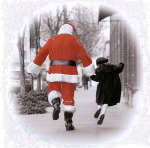 A man in a Santa suit walks down a sidewalk with a little girl.