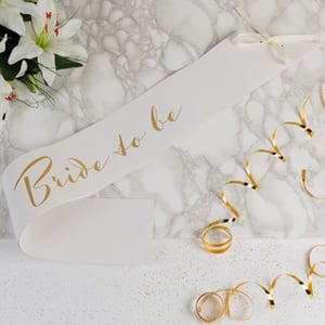 A white sash that says "bride to be" on it.