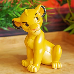 A figurine of Simba from The Lion King sits on a wooden table.