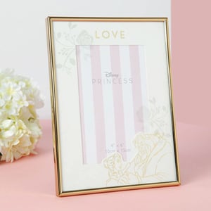 A Disney princess picture frame is sitting on a pink table.