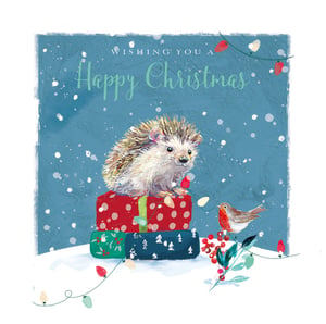 A Happy Christmas card with a hedgehog on top of a pile of presents.