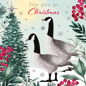 A Christmas card with two geese in front of a Christmas tree.