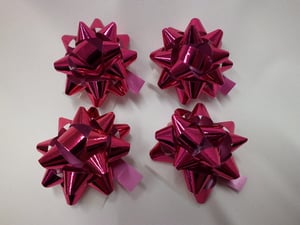 Four pink bows with pink ribbons are on a white surface.