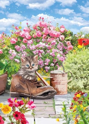 A kitten sits in a boot in a garden surrounded by flowers.