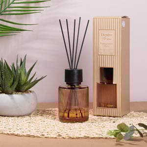 a desire aroma pomegranate noir reed diffuser sits on a table next to a plant