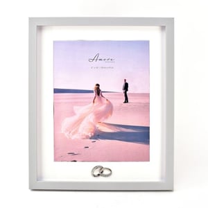 a picture of a bride and groom in the sand with wedding rings in a frame .