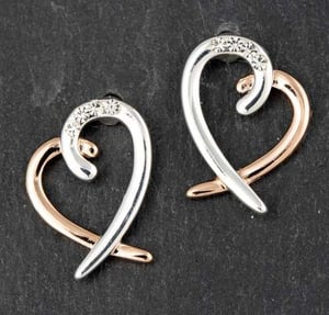 a pair of silver and rose gold heart shaped earrings on a black surface .