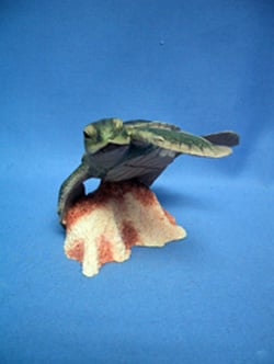 A sea turtle is sitting on a rock, on a blue surface.